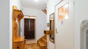 Eine Holztreppe führt zu einer dunklen Holztür, ein kleines Holzregal und ein 'Nichtraucher'-Schild an der Wand.