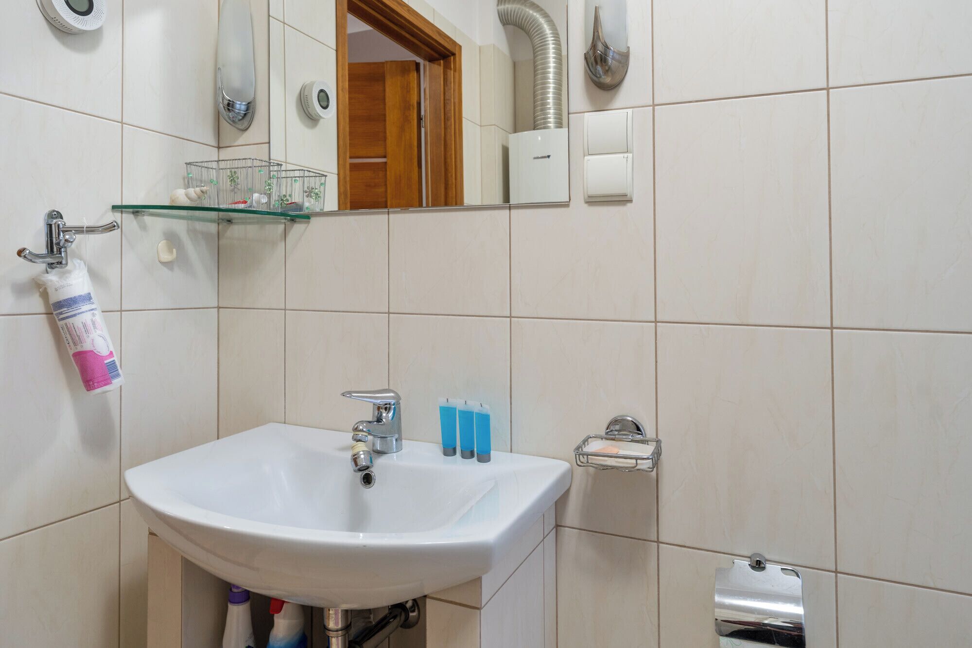 Une salle de bain avec un lavabo blanc, un miroir, une étagère en verre où sont rangés les articles de toilette et un espace douche.
