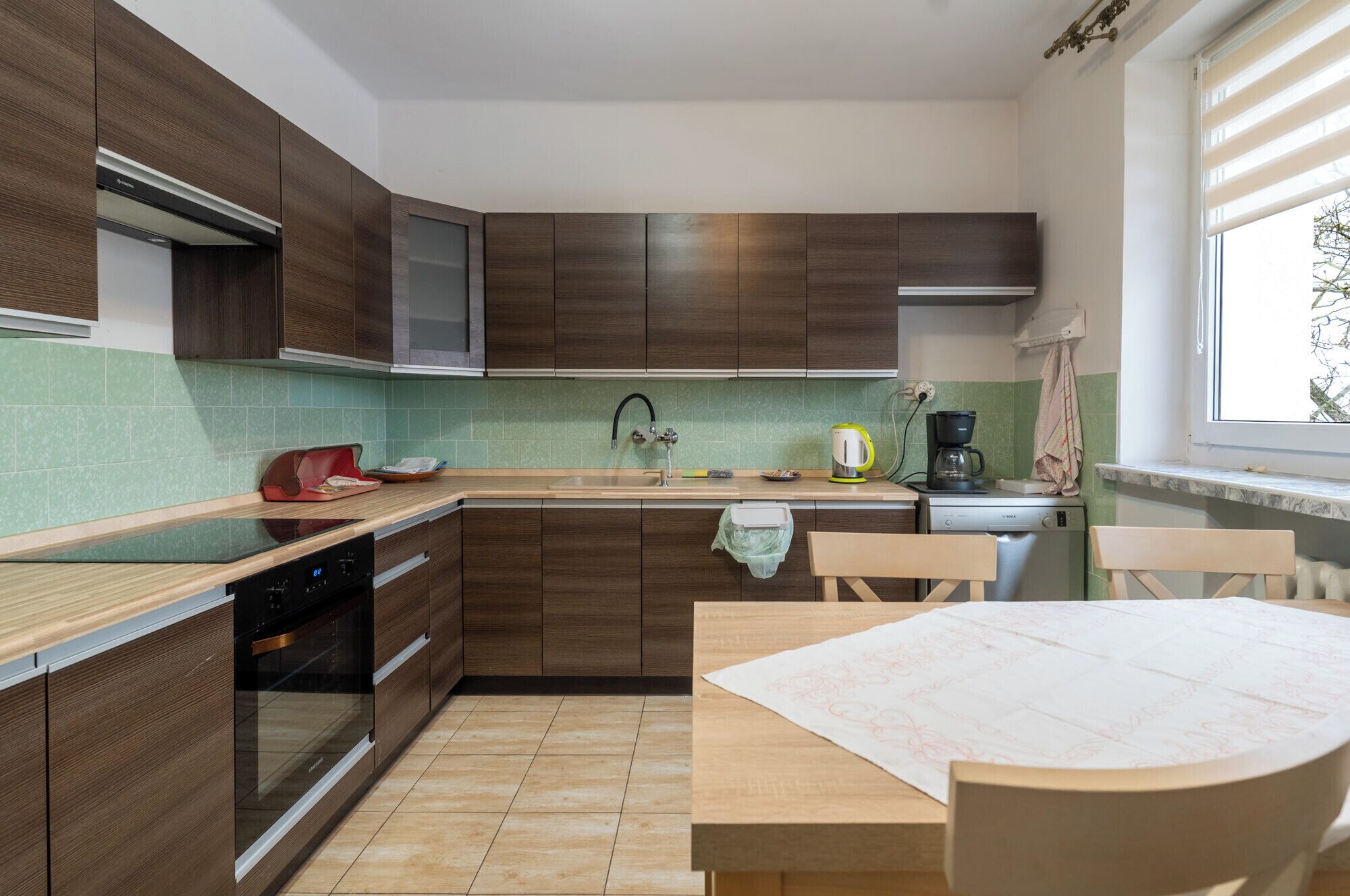 A modern kitchen with wooden cabinets, a built-in oven, a sink, and a dining area with a table and chairs.