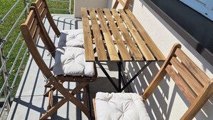 Eine Terrasse mit Holztisch und -stühlen, einem Metallgeländer und einem Gebäude im Hintergrund.