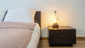 Ein ordentlich bezogenes Bett mit einer rosa Decke und einem Nachttisch mit einer Lampe.