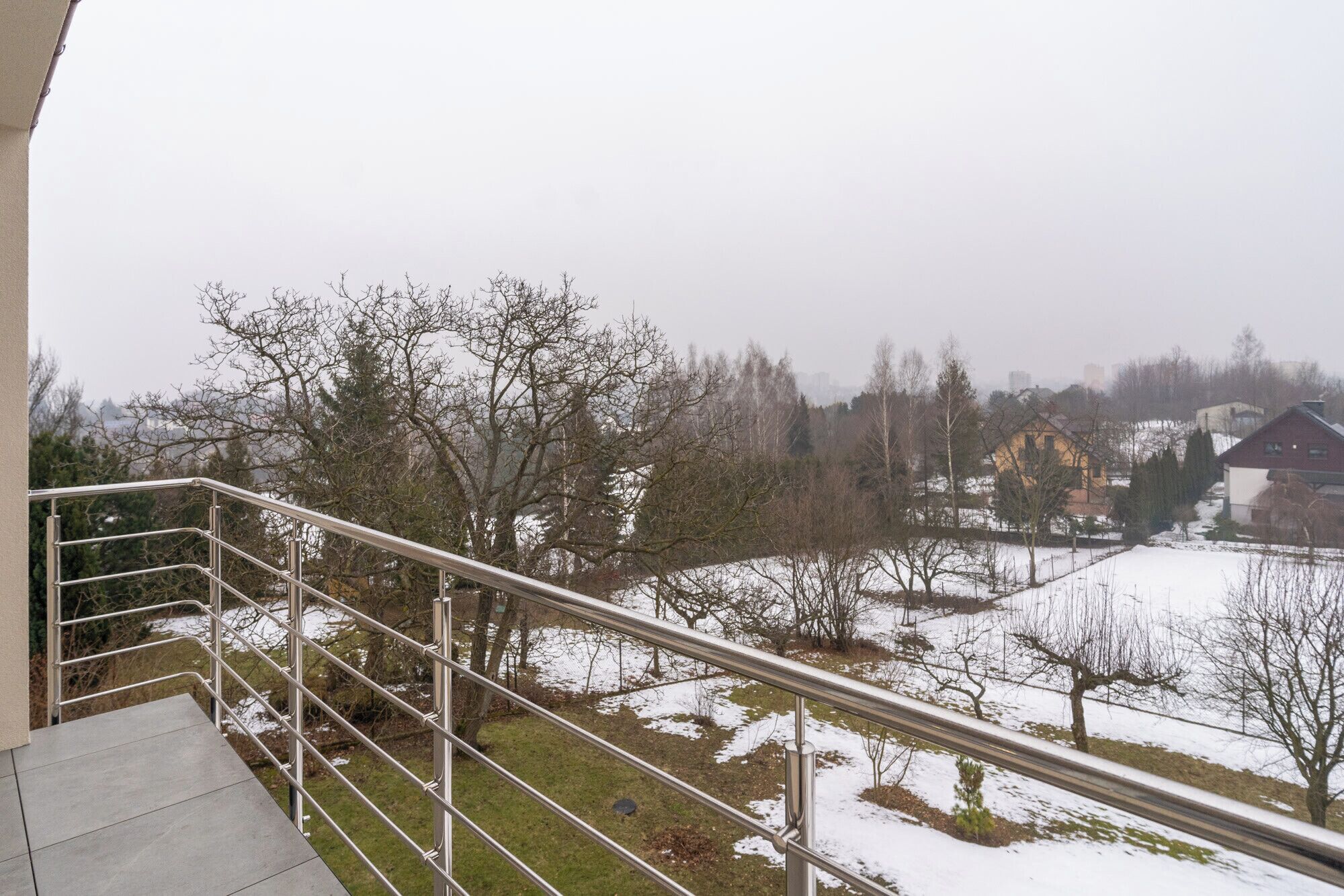 A balcony with a metal railing overlooking a snowy landscape with trees and houses.