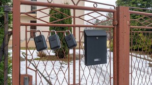 Een poort ingangen met een metalen hek, drie hangsloten en een stroomkast.