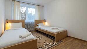 Een slaapkamer met twee houten bedden, een groot raam met gordijnen en een kamerbreed tapijt met een patroon.