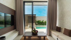 A modern living room with a large window, a dining table with a fruit bowl, and a sofa. - Villa Fresko 5 by Alfred in Bali (Munggu)