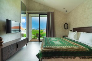 A modern hotel room with a large bed, a flat-screen TV, a balcony with a view of the landscape, and a dining area. - Villa Fresko 5 by Alfred in Bali (Munggu)