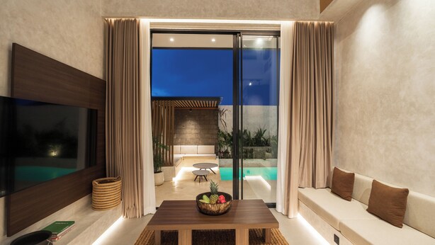 A modern living room with a wooden table, a sofa, and a large TV. There is a sliding glass door leading to a balcony with a pool. - Villa Fresko 5 by Alfred in Bali (Munggu)