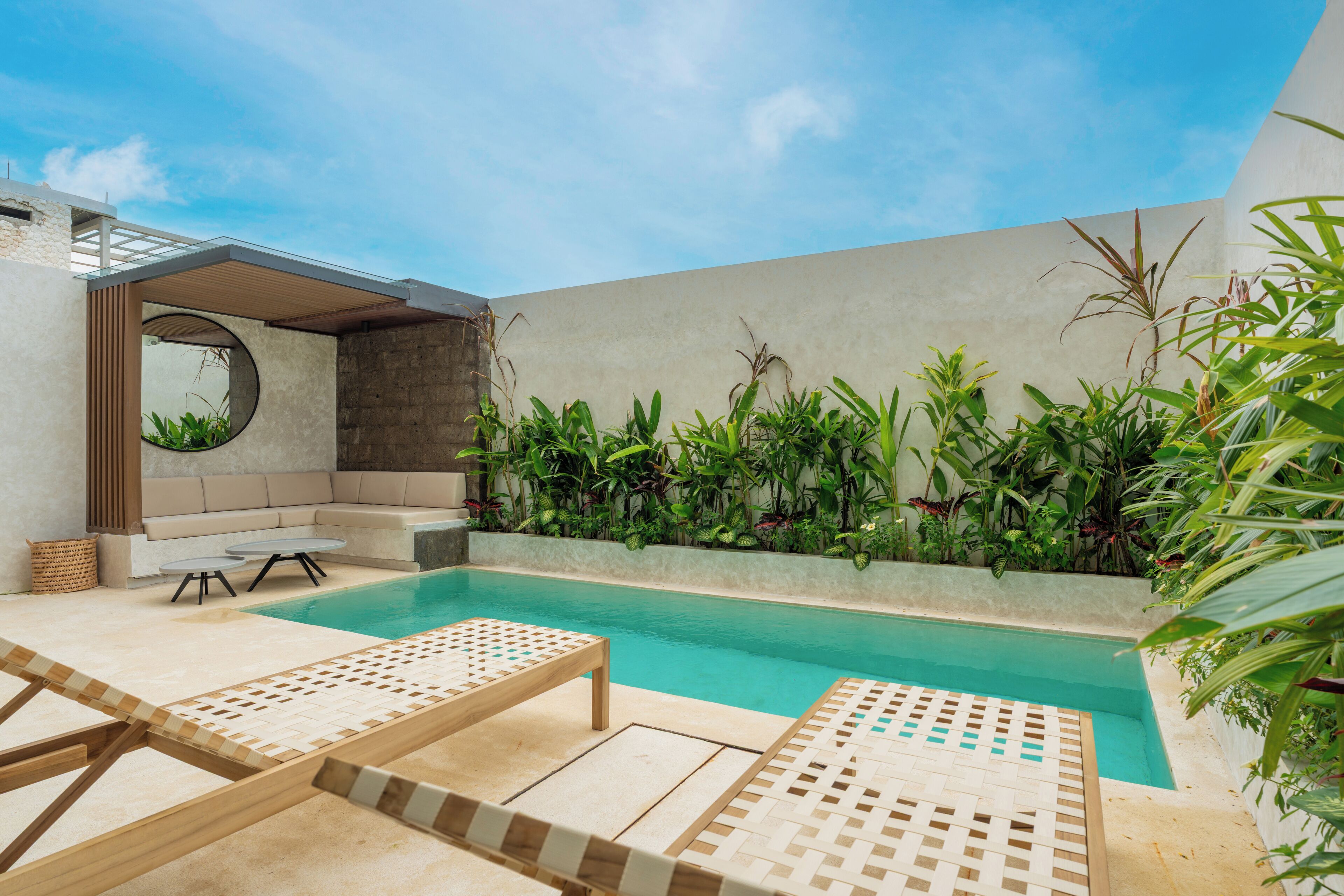A modern outdoor pool area with lounge chairs, a seating area, and lush greenery.