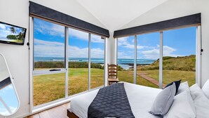 Een slaapkamer met een groot bed, een stoel en een televisie. Het heeft uitzicht op de oceaan en een grasachtig landschap.