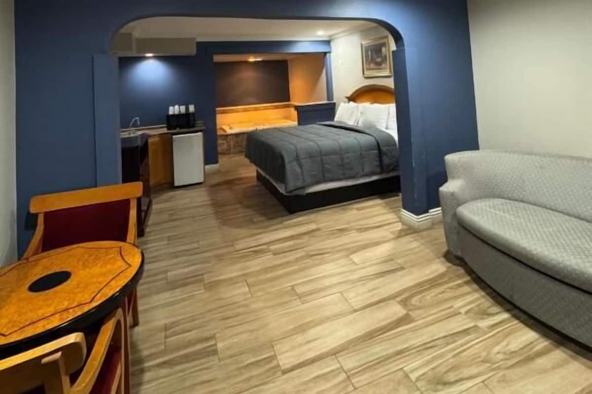 Una habitación de hotel compacta con cama, sofá, una mesita y kitchenette.