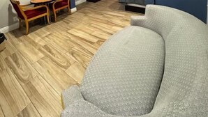 A modern living room with a grey sofa, a wooden dining table with red chairs, a kitchen area with a TV, and a large mirror on the wall. - Sunset inn &Suites (Gardena)