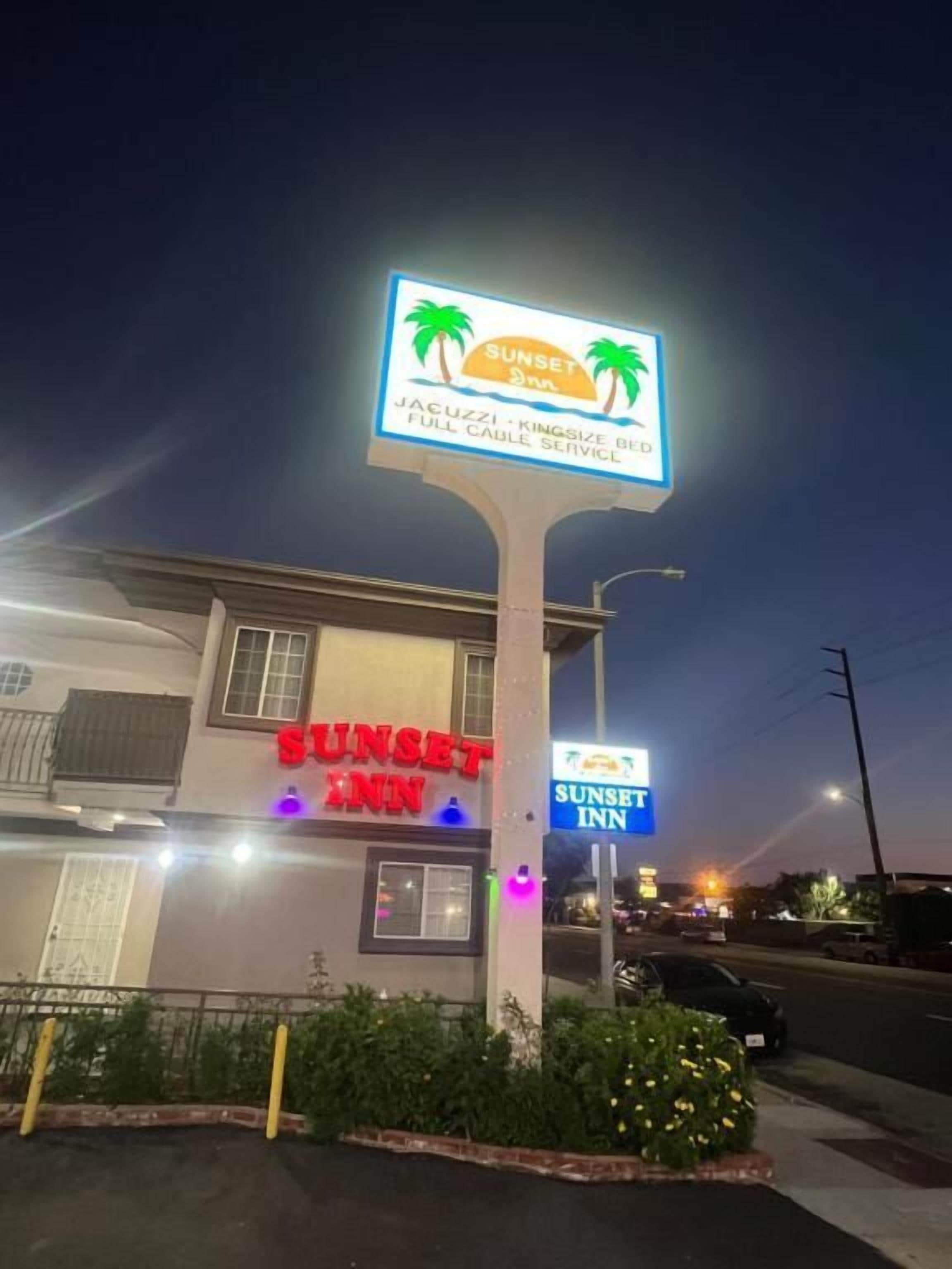 A building with a sign for Sunset Inn, featuring palm trees and a sun.