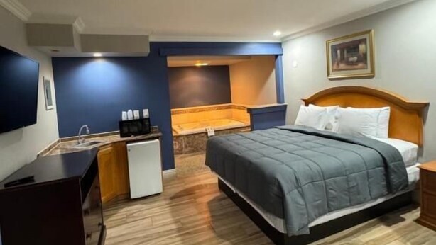 A bedroom with a bed, bedside table, and a small desk with a chair. - Sunset inn &Suites (Gardena)