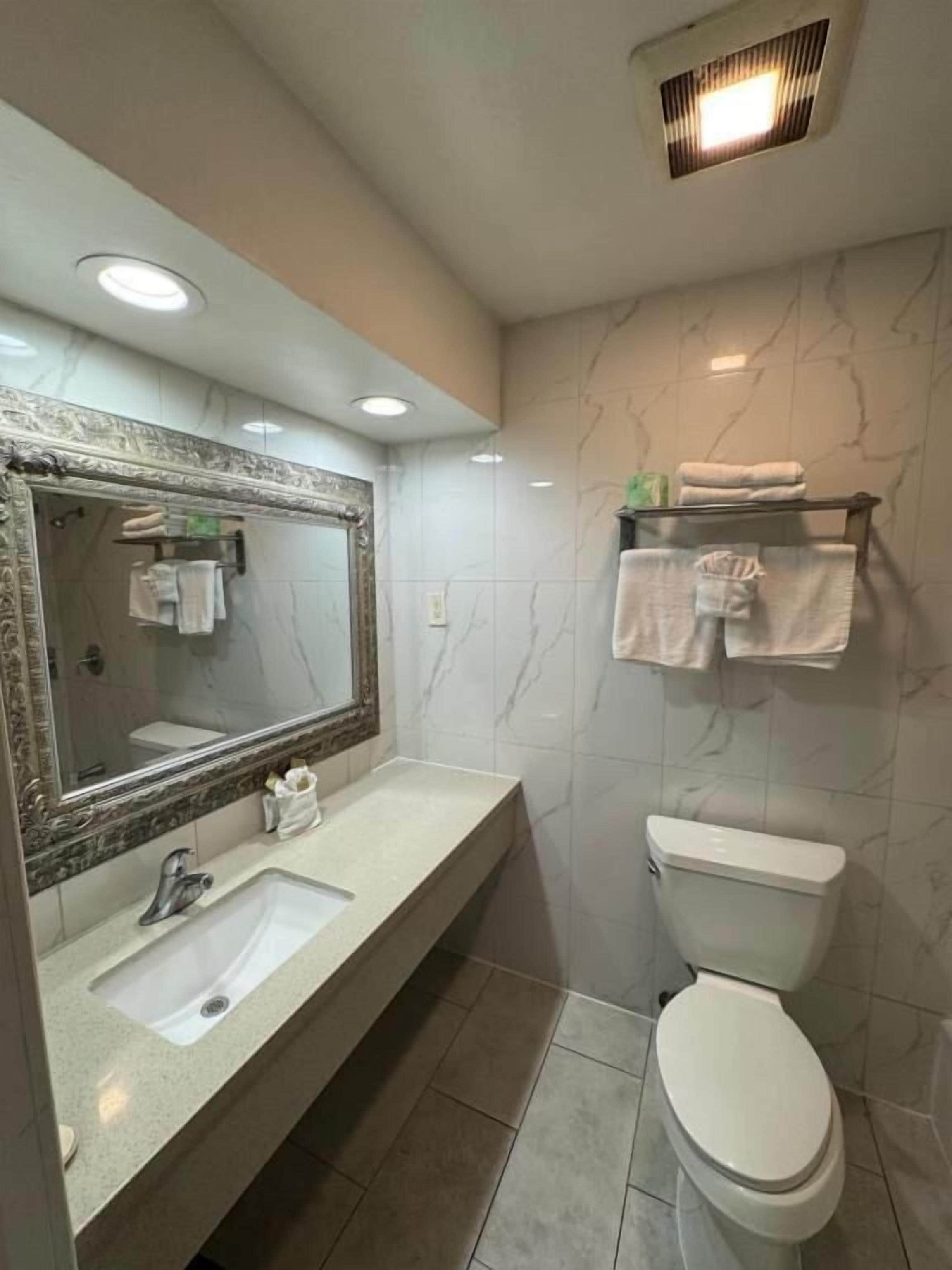 Un baño con pared de mármol, un lavabo con espejo, un inodoro y un estante con toallas.