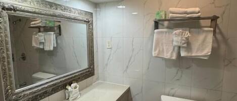 Un baño con pared de mármol, un lavabo con espejo, un inodoro y un estante con toallas.