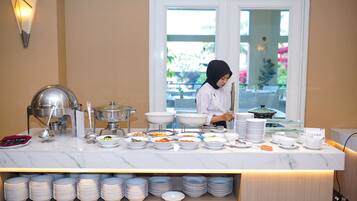 A buffet setup with various dishes and serving utensils, a buffet server, and a view of the outdoors through a glass door.