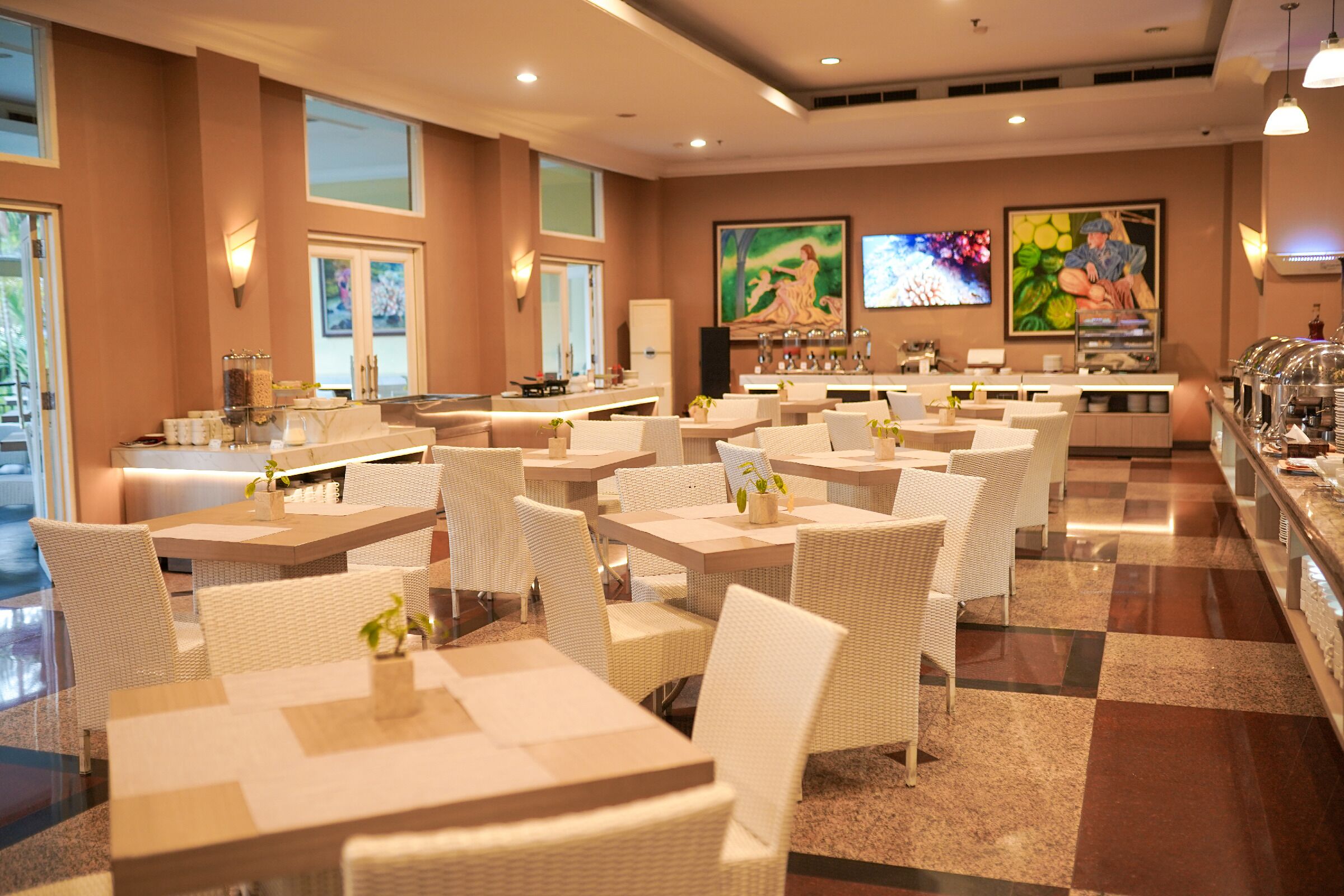 A spacious dining area with multiple tables and chairs, large windows, and artwork on the walls.