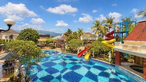 Una piscina con diseño de cuadros, rodeada de palmeras y un tobogán.