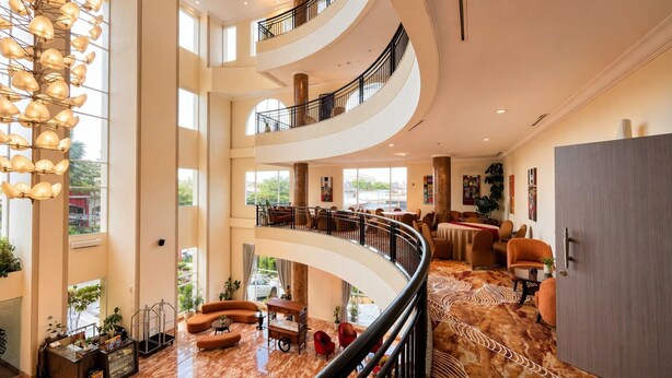 Un vestíbulo de hotel de varios niveles con una escalera curva, zonas de estar y ventanas amplias.
