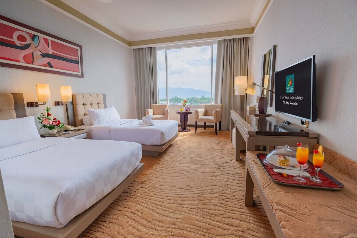 Habitación de hotel con dos camas, un televisor, un escritorio y una bandeja de comida, y vistas a las montañas.