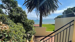 Una escalera lleva a un balcón con vista a una playa, palmeras y cielo despejado.