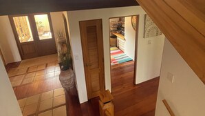Interior de madera con varios niveles, una escalera, vista a una sala de estar y una puerta que da a otra habitación.