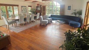 Un salón espacioso con piso de madera, un comedor con mesa y sillas, un sofá azul y ventanas amplias con vistas a zonas verdes.
