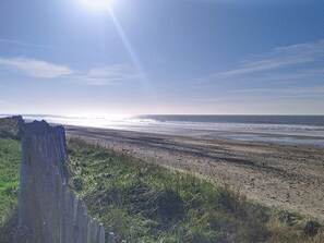 A beach with a wooden fence and grassy area in the foreground. - Le Chalet by Interhome (Bretteville sur Ay)