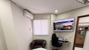 Una camera da letto con un letto, una scrivania con un computer, una sedia, una televisione e una finestra con persiane.