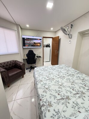 A bedroom with a bed, a desk, a chair, a sofa, a TV, and a fan. - Full suite with air conditioning, Wi-Fi, and Netflix. (Vitória)