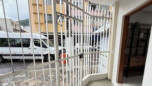En balkon med gelænder, en hvid varevogn parkeret udenfor, og en bygning med flere vinduer i baggrunden.
