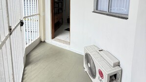 Et værelse med hvidt loft, et vindue med persienner, en hvid aircondition og en dør til et andet værelse.