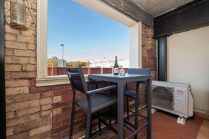 Un balcon avec une table et des chaises, une fenêtre donnant sur des immeubles et un appareil de climatisation.