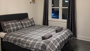 A bedroom with a bed, a hanging light fixture, a window with curtains, and a small shelf with a plant. - Wonderful 1-bed apt East London central (London)