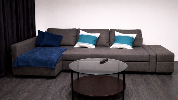 A grey sofa with blue and white pillows, a blue throw blanket, and a glass coffee table with a remote control on it. - Wonderful 1-bed apt East London central (London)