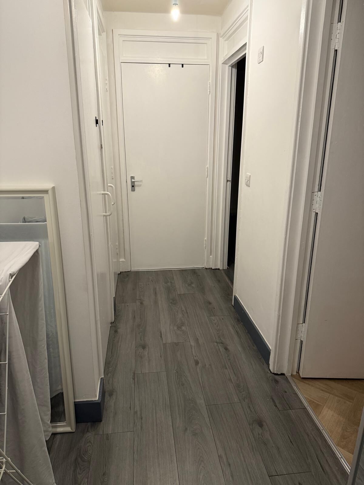 A narrow hallway with a wooden floor, white walls, and a closed door at the end.
