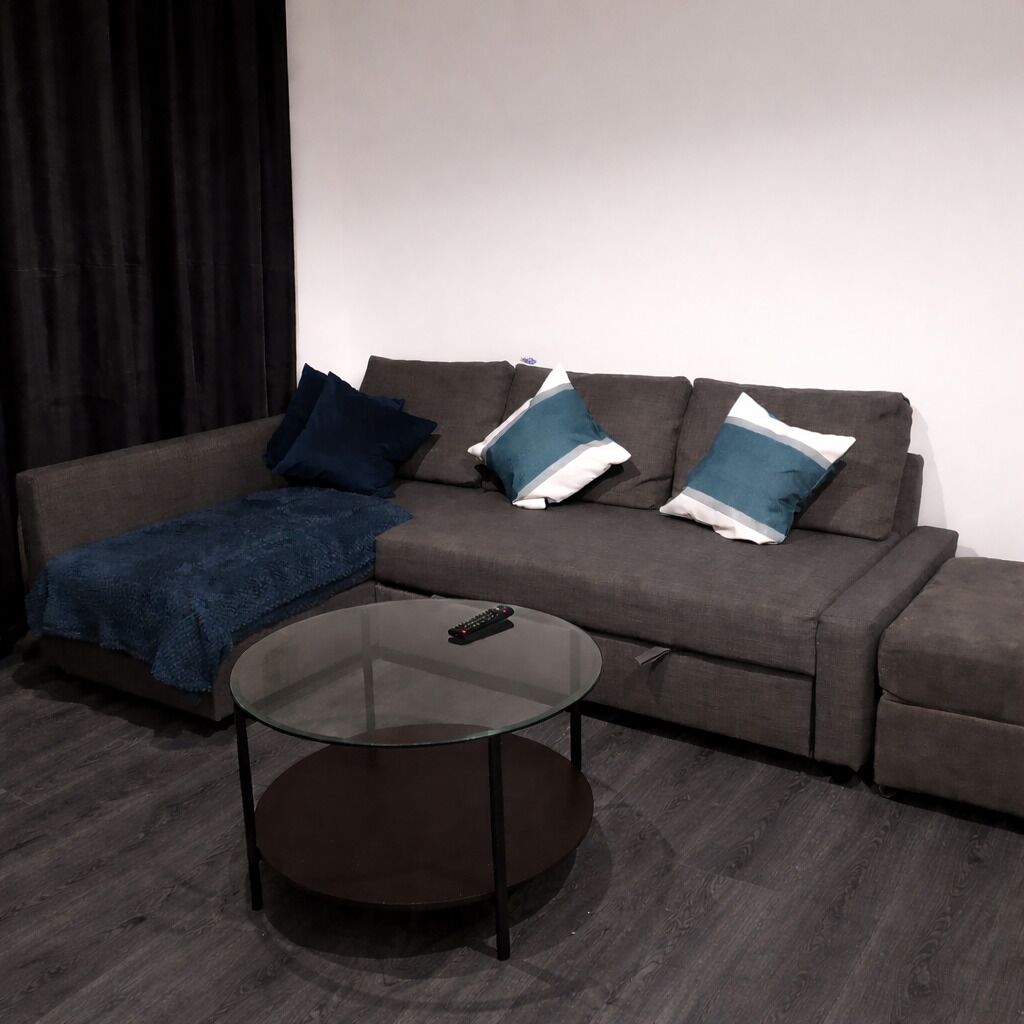 Uma sala de estar com um sofá, uma mesa de centro de vidro e um controle remoto sobre a mesa.