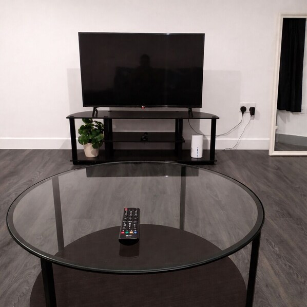 Un salon moderne avec une table basse en verre, une télécommande, un téléviseur à écran plat, un meuble de rangement noir et une plante en pot.