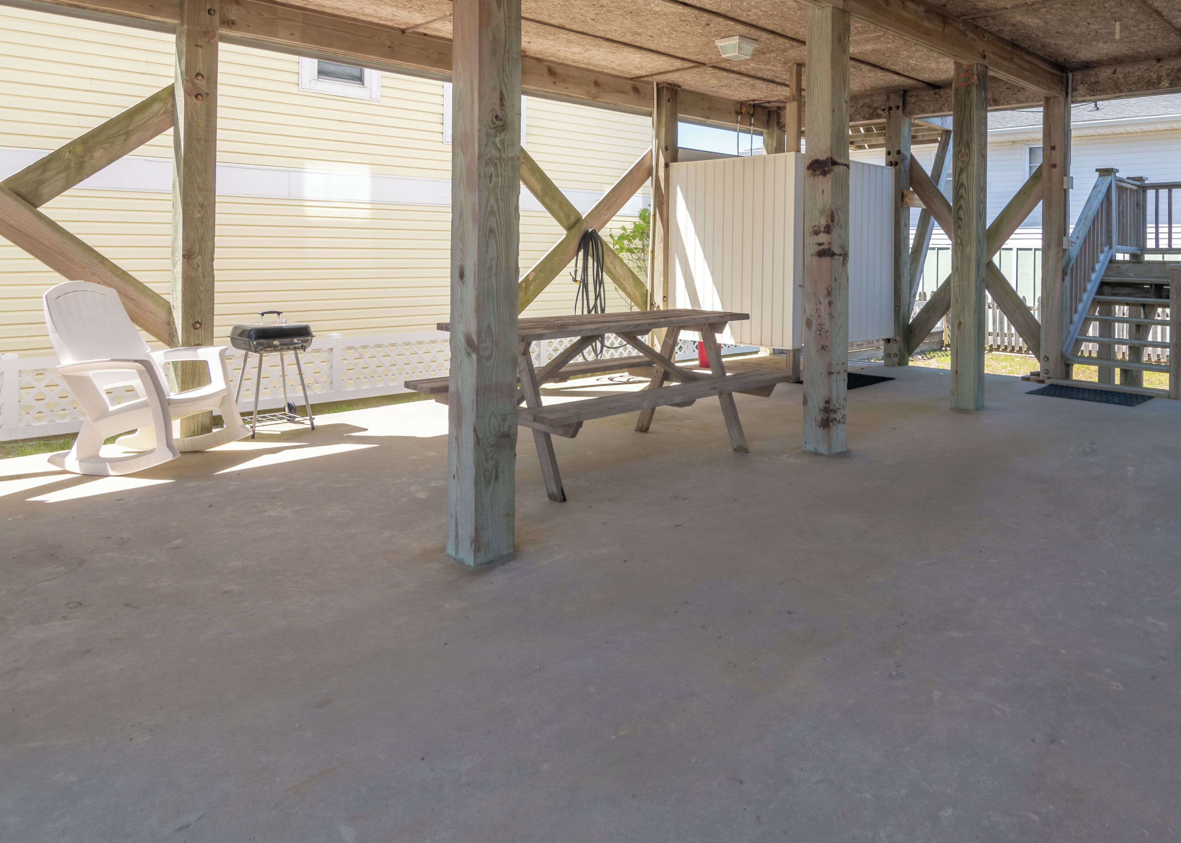 Un espace extérieur abrité, doté d’une table de pique-nique et de chaises, de poutres en bois et d’une clôture blanche.