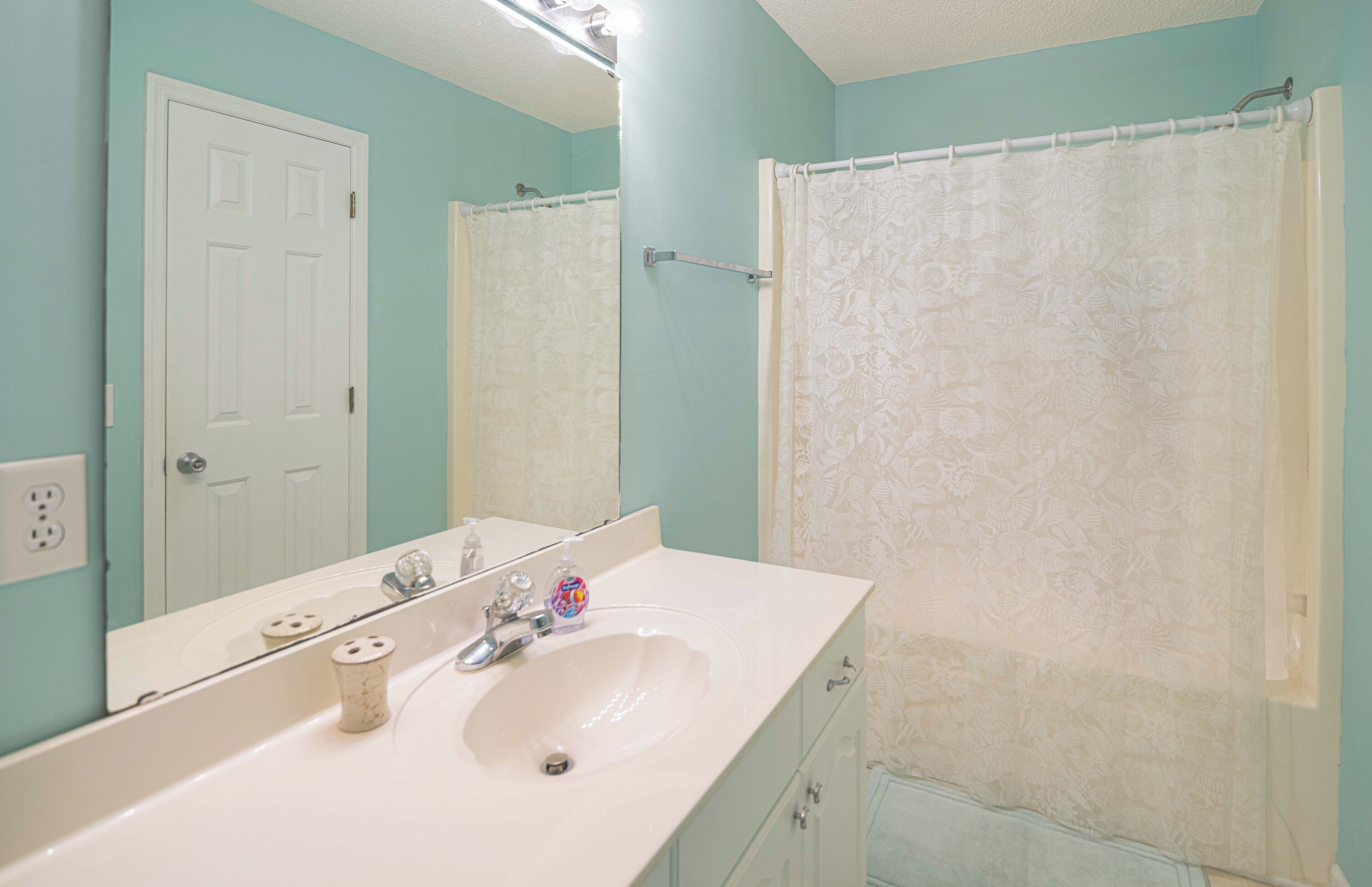 A bathroom with a white sink, mirror, and shower curtain.