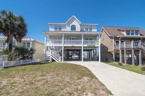 A two-story beachfront house with a balcony, a covered porch, and a staircase leading to the upper level. - Bel Chateau - Beach access, Wifi, comfy beds, and much more! (Holden Beach)