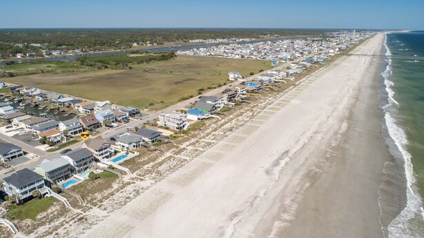 Vista aérea de uma área residencial costeira, com casas, uma praia e um cais.