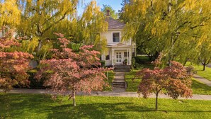 A two-story house with a front porch, surrounded by trees with autumn foliage. - Gorgeous 1902 Craftsman-EV Charger-Lush Grounds-Walk to Main Street-Dogs OK (Walla Walla)