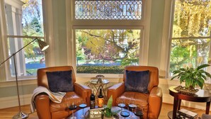 A room with two leather armchairs, a coffee table with wine glasses, a potted plant, and a view of a garden through a window with a stained glass design. - Gorgeous 1902 Craftsman-EV Charger-Lush Grounds-Walk to Main Street-Dogs OK (Walla Walla)