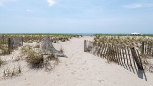 Un sendero arenoso en la playa, con cercas de madera y vegetación escasa.