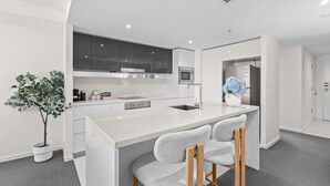 A modern kitchen with a central island, grey chairs, and a potted plant. - Hilton 2BR Retreat Sky High Ocean Views Pool (Surfers Paradise)