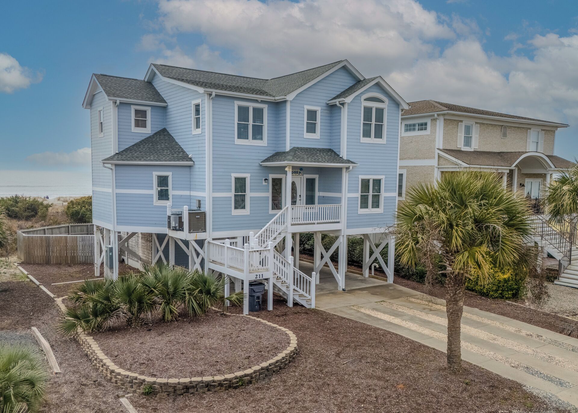 Une maison à deux étages située en bord de mer, dotée d’un balcon et d’une véranda couverte.