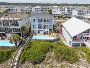 A beachfront property with a swimming pool, multiple balconies, and a view of neighboring houses. - Hobbs Realty - The Roost: Spacious 5-Bedroom, Private Pool, Elevator, $250 Beach Gear Credits (Holden Beach)