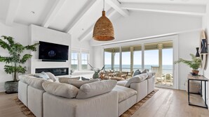 Un soggiorno moderno con un ampio divano componibile, una televisione a schermo piatto e una grande finestra con vista sull'oceano.