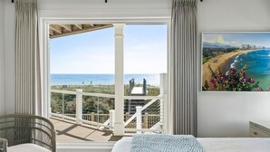 Una camera da letto con un'ampia finestra vista spiaggia, una sedia in vimini e un quadro raffigurante una spiaggia.